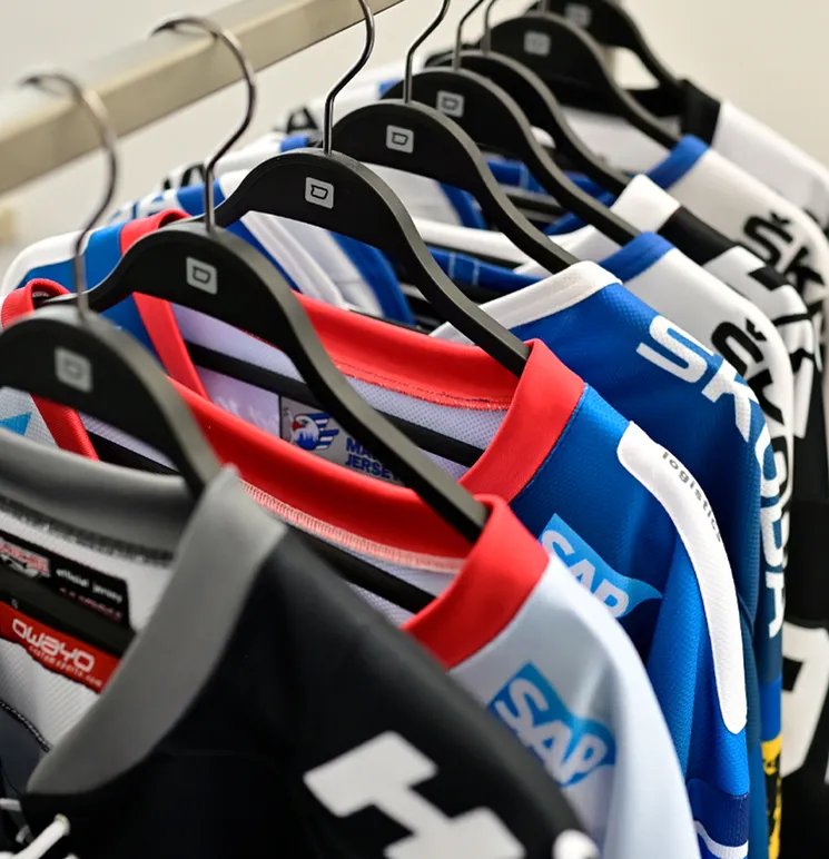 Una fila de camisetas deportivas coloridas personalizadas de owayo cuelgan de perchas negras en un perchero.