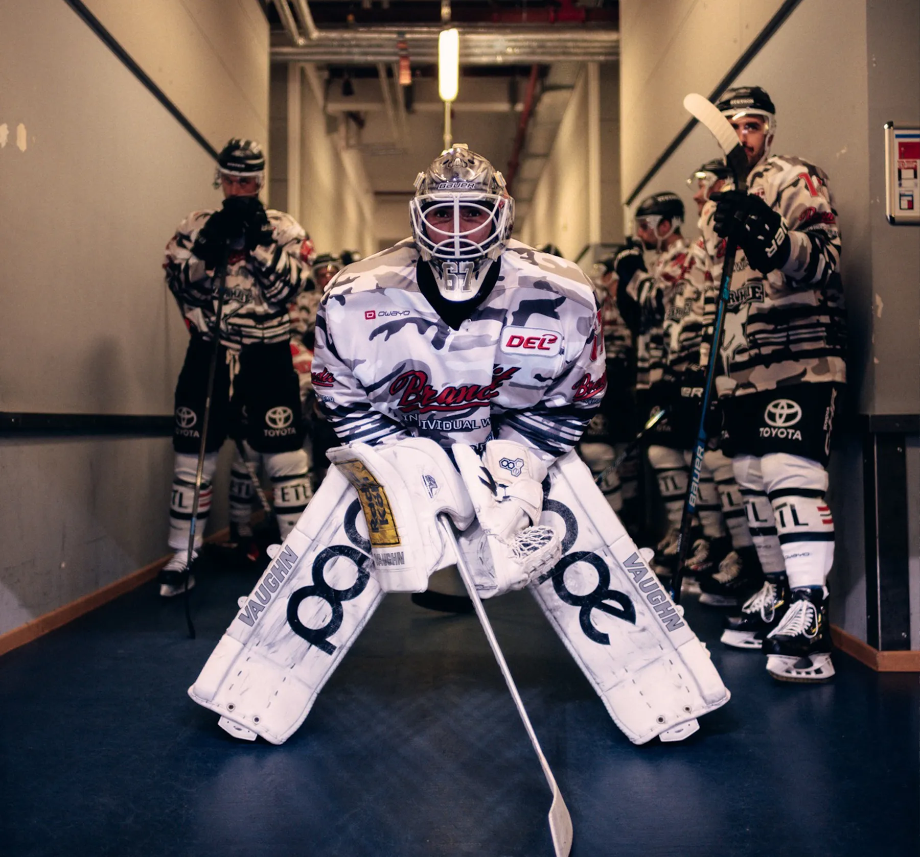 Un portero de hockey con un uniforme llamativo está listo, mientras otros jugadores esperan detrás de él.