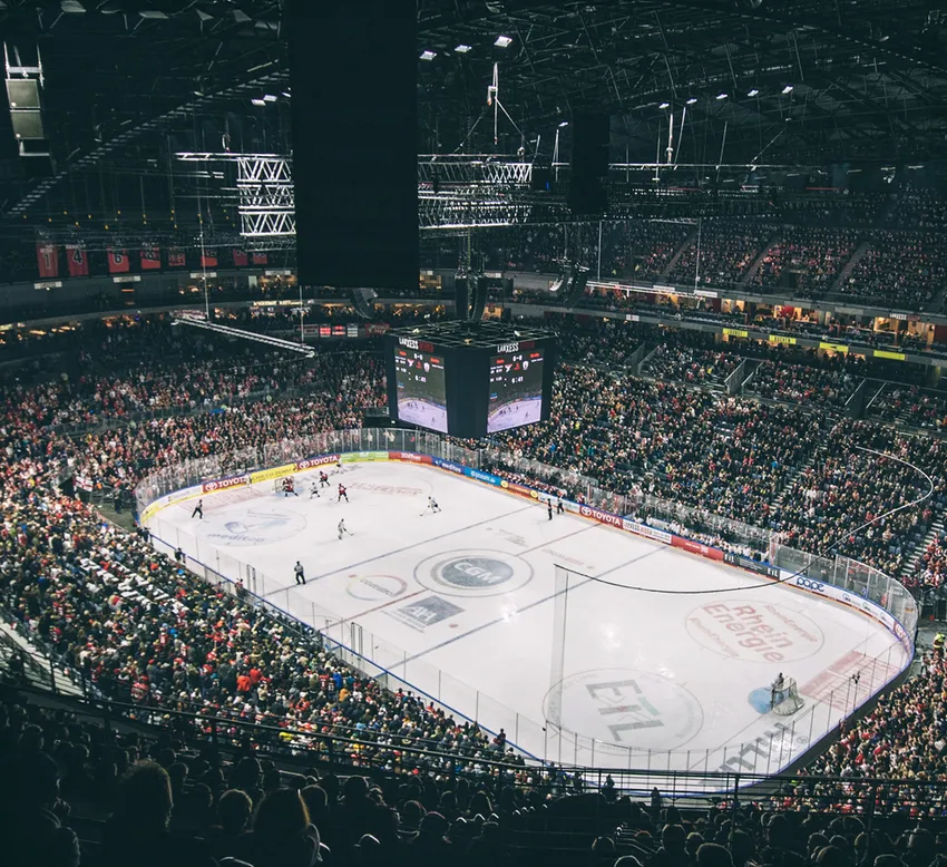 Una vista amplia de un estadio de hockey sobre hielo lleno, con jugadores en el hielo y un gran marcador.