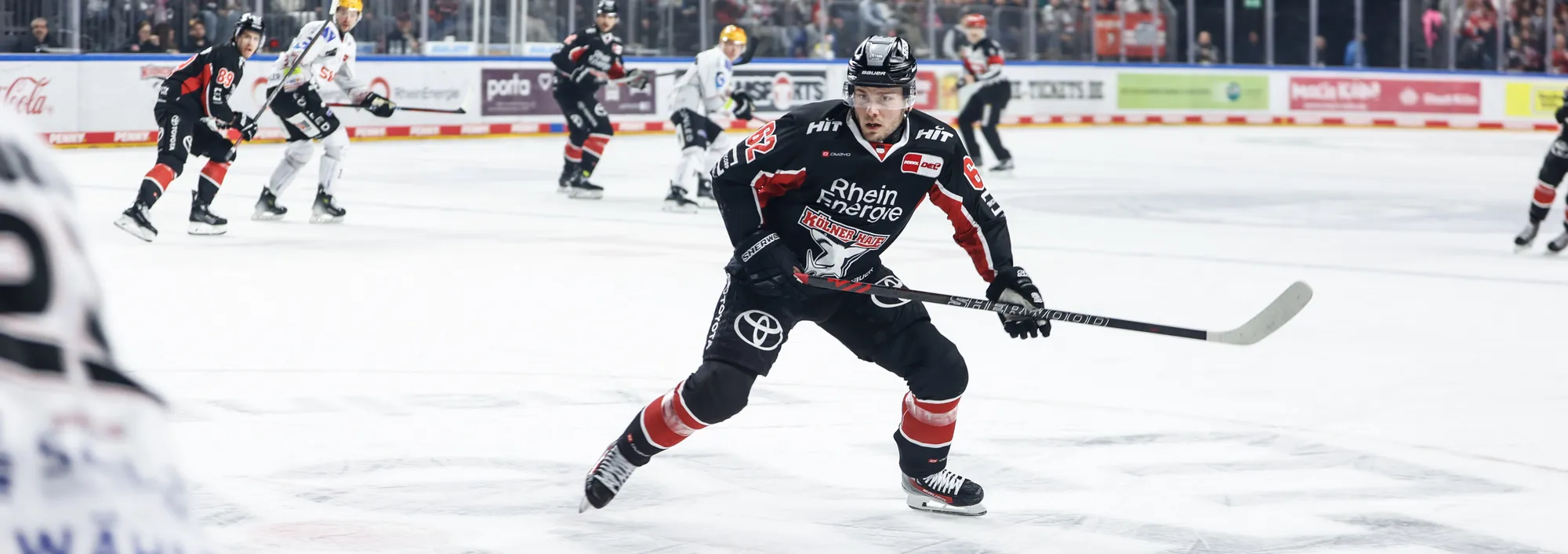 Un jugador de hockey sobre hielo con una camiseta negra y roja patinando sobre el hielo con un palo de hockey.