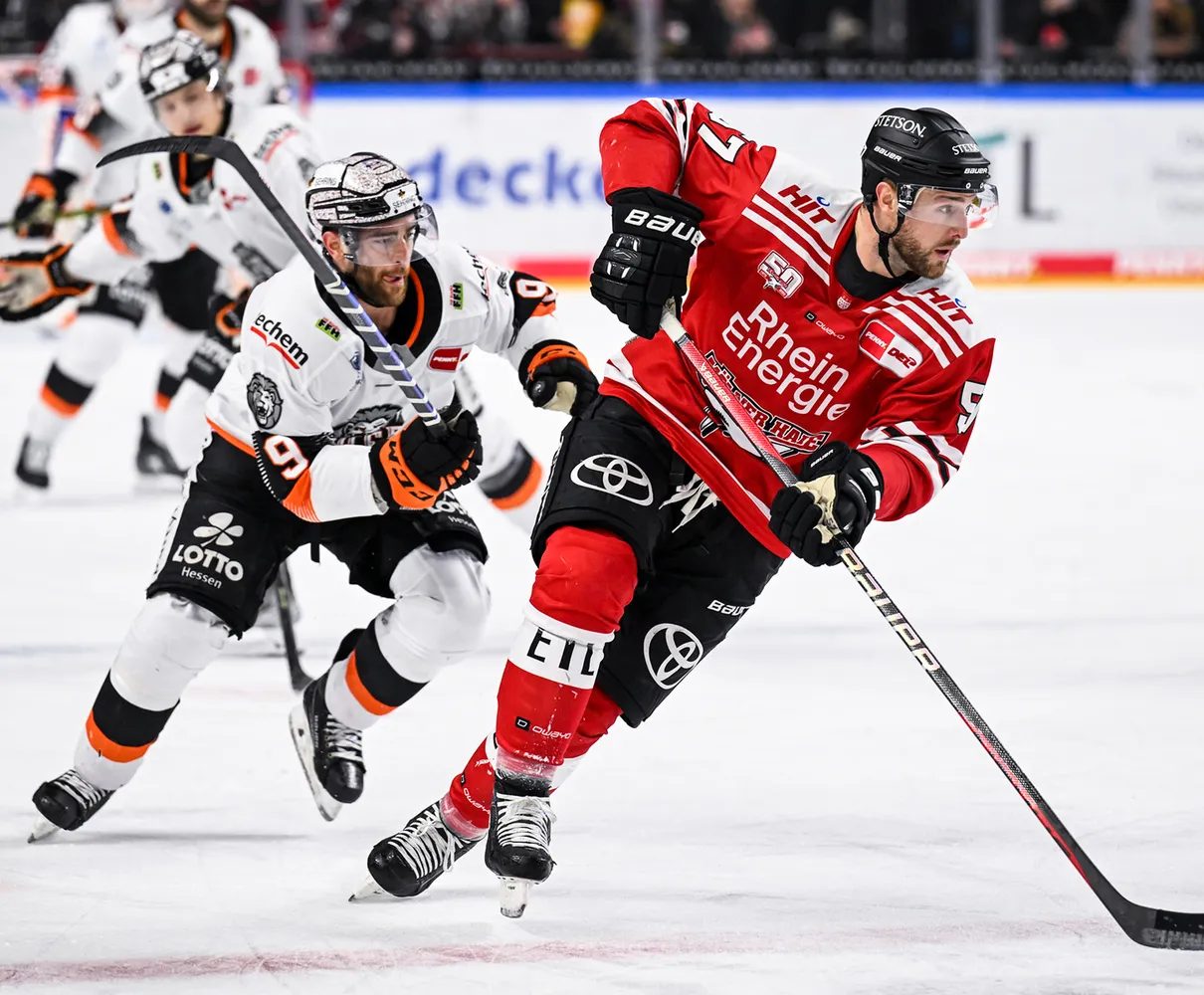 Dos jugadores de hockey sobre hielo en el hielo, uno con un jersey rojo y el otro con un jersey blanco con acentos naranjas.