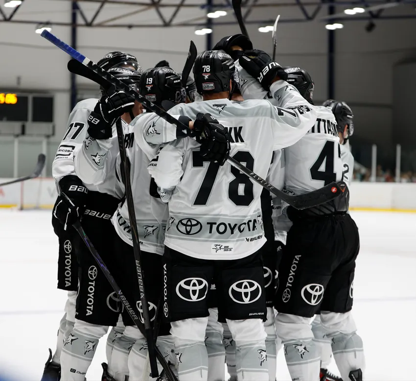 Jugadores de hockey sobre hielo con uniformes blancos con números negros y el logo de Toyota celebran en la pista de hielo.