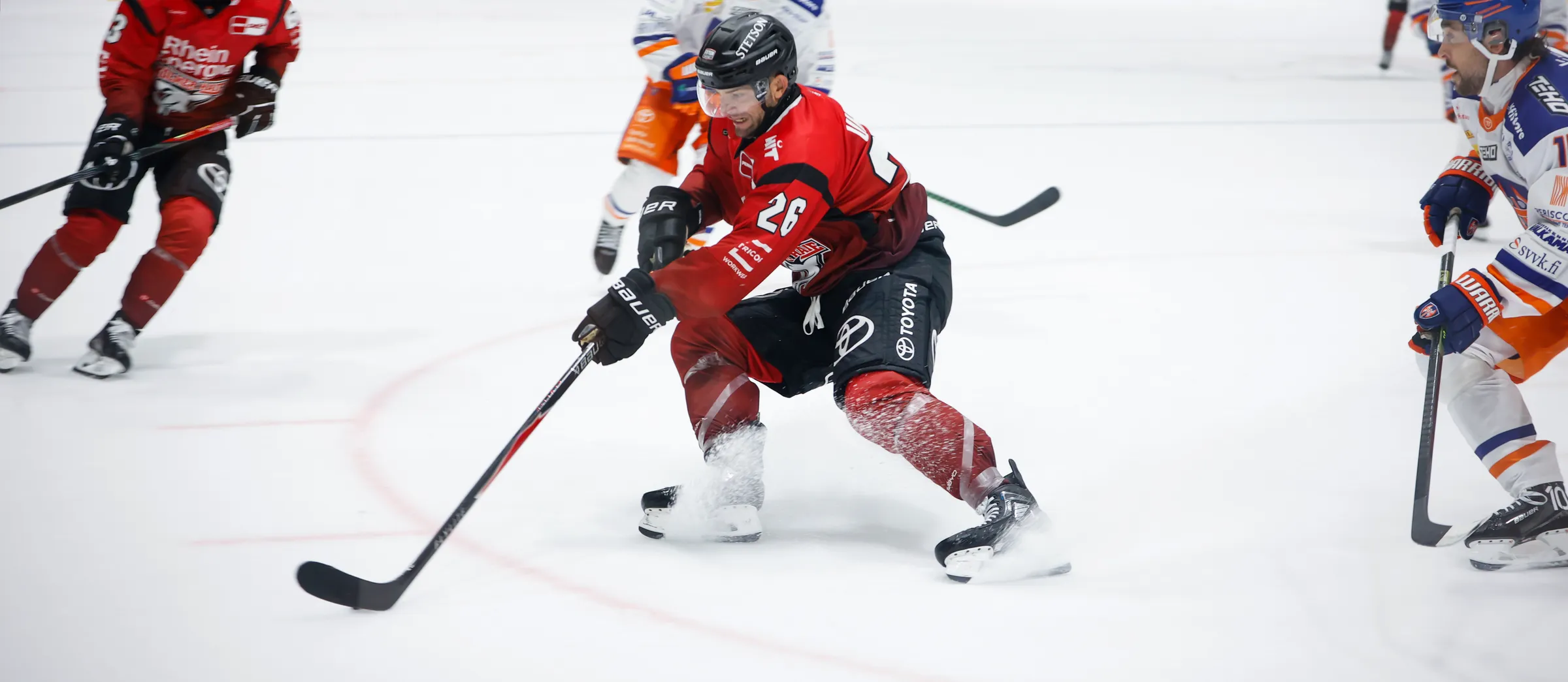Un jugador de hockey sobre hielo con ropa deportiva roja está driblando el puck sobre el hielo.