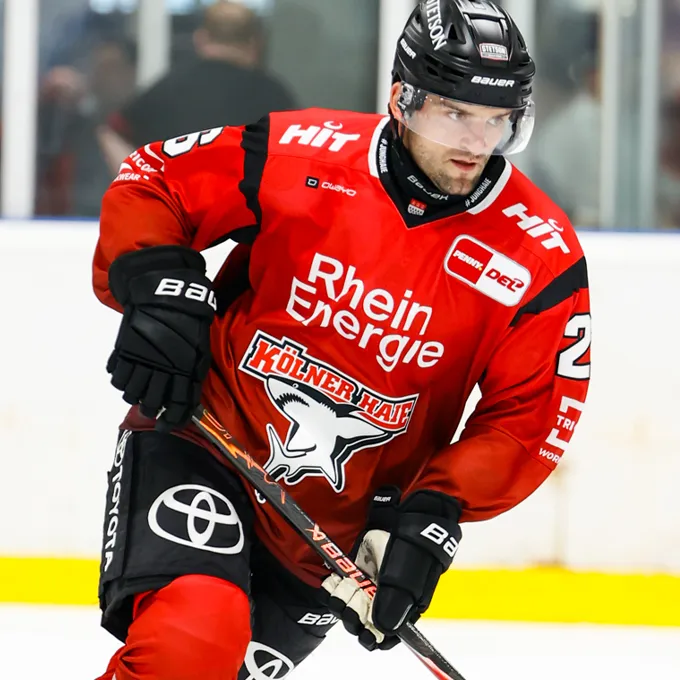 Un jugador de hockey sobre hielo con un jersey rojo con el logo de Rhein Energie y Kölner Haie, sobre el hielo.