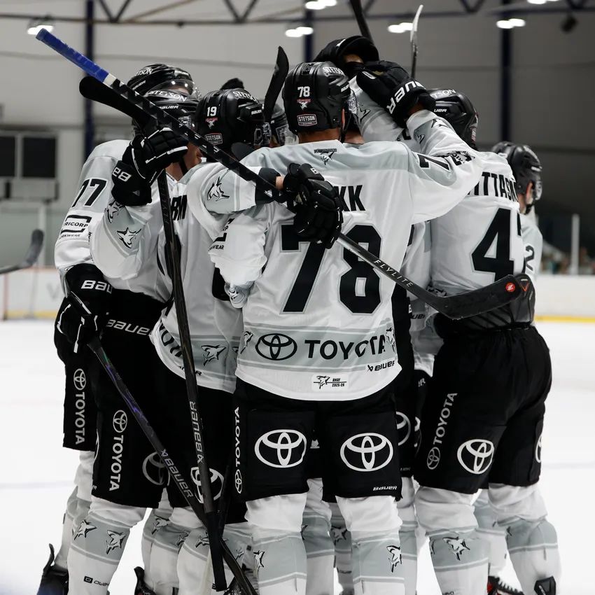 Un grupo de jugadores de hockey sobre hielo con camisetas blancas y negras abrazándose sobre el hielo.