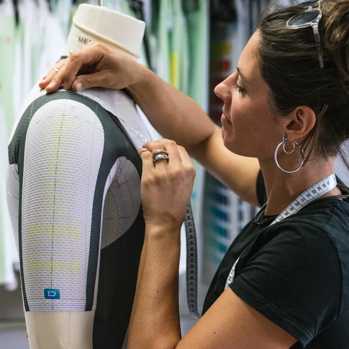 Una mujer ajusta una prenda deportiva personalizada en un maniquí mientras lleva una cinta métrica.
