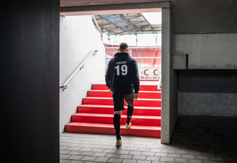 Un futbolista con una sudadera negra con el número 19 y pantalones cortos sube las escaleras rojas de un estadio.