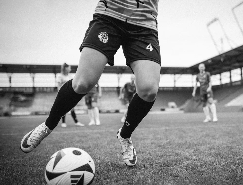 Una jugadora de fútbol con pantalones cortos y calcetas largas jugando con un balón en el campo.