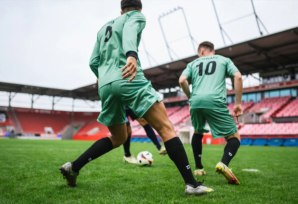 Dos futbolistas con camisetas verdes y calcetines negros jugando en un campo de césped.