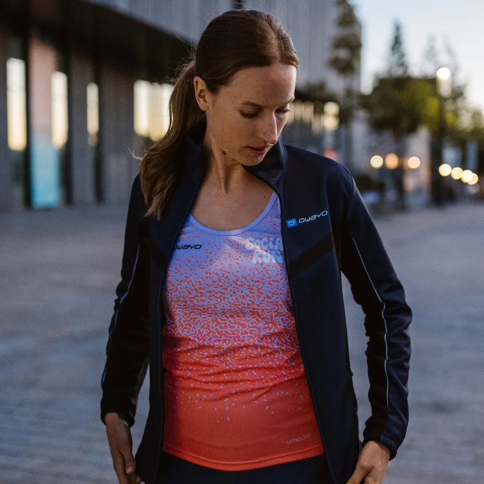 Una mujer lleva una chaqueta deportiva y una camiseta sin mangas colorida con un diseño moderno mientras está de pie en una calle urbana.