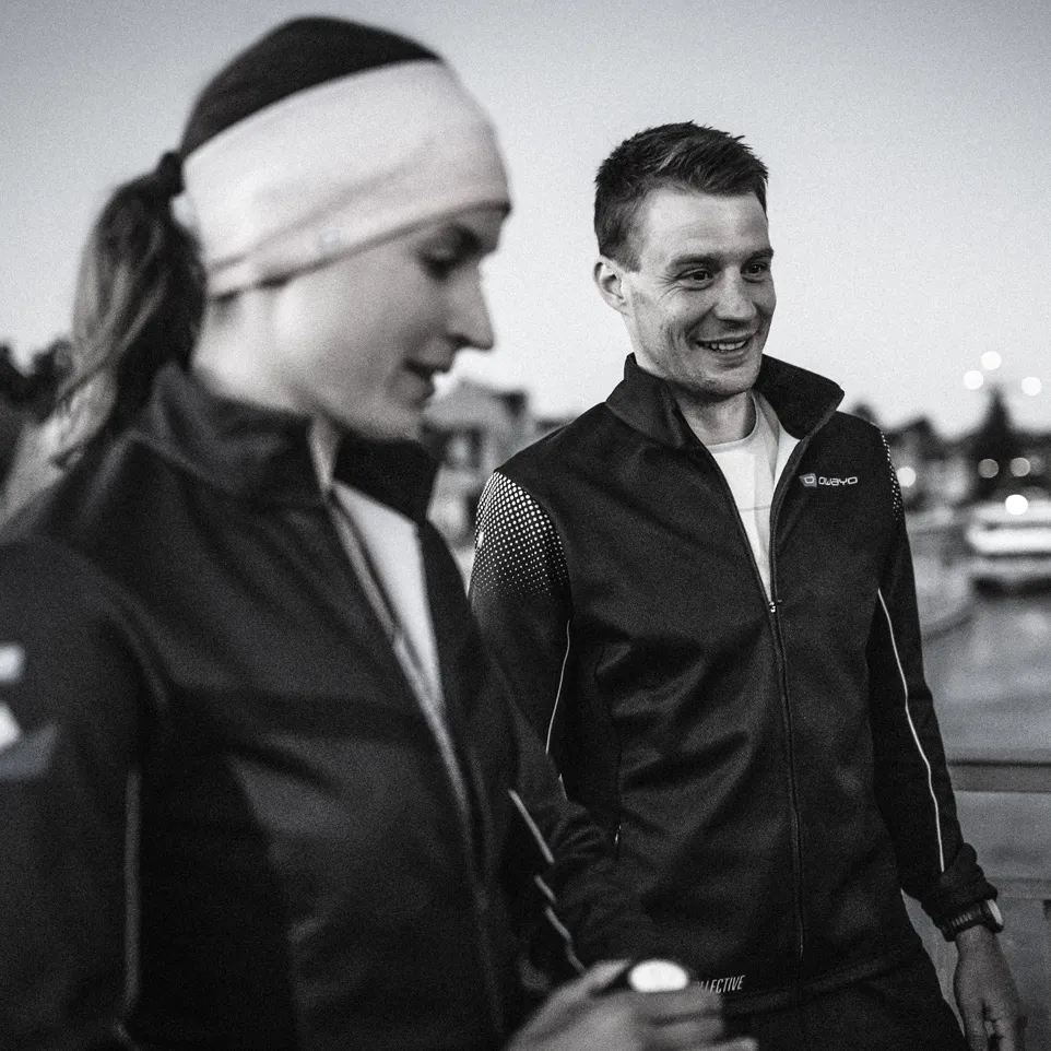 Dos atletas con chaquetas negras modernas están al aire libre, sonriendo y listos para entrenar.
