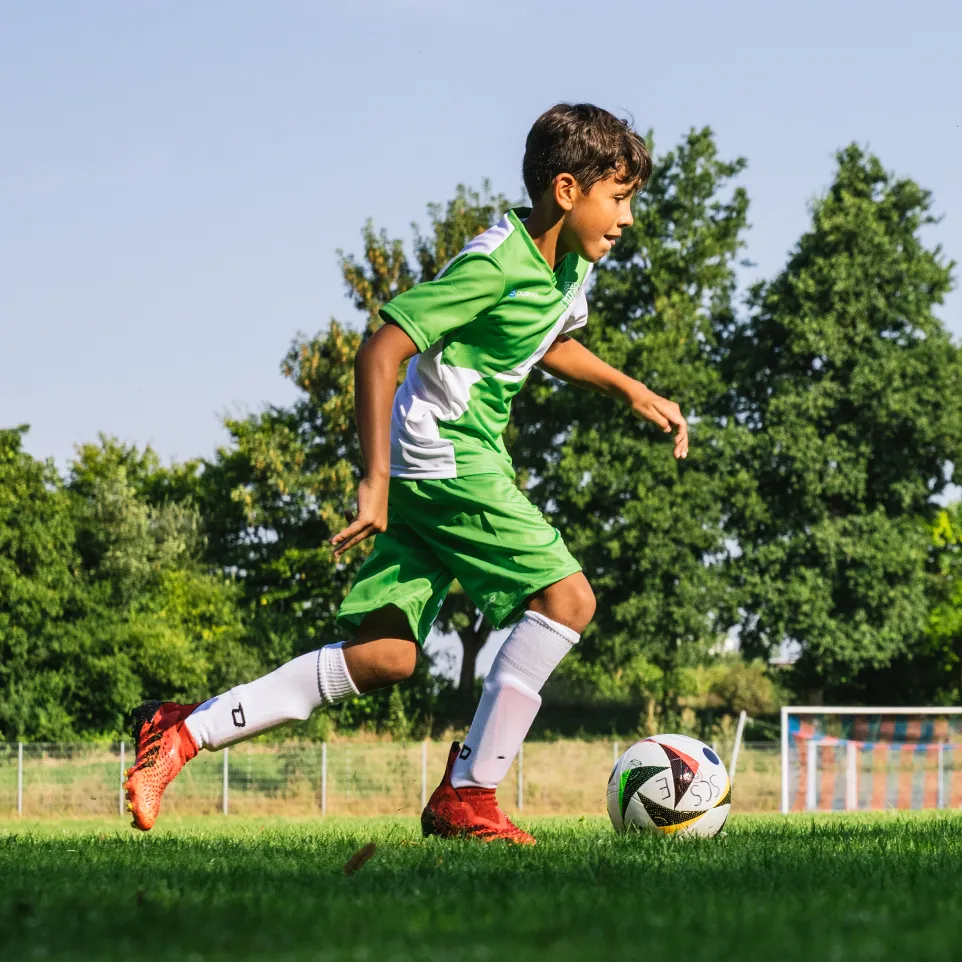 Un joven futbolista con ropa deportiva verde y blanca corre en un campo de fútbol.