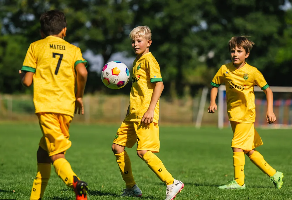 Tres niños con camisetas de fútbol amarillas brillantes están jugando en un campo de hierba.