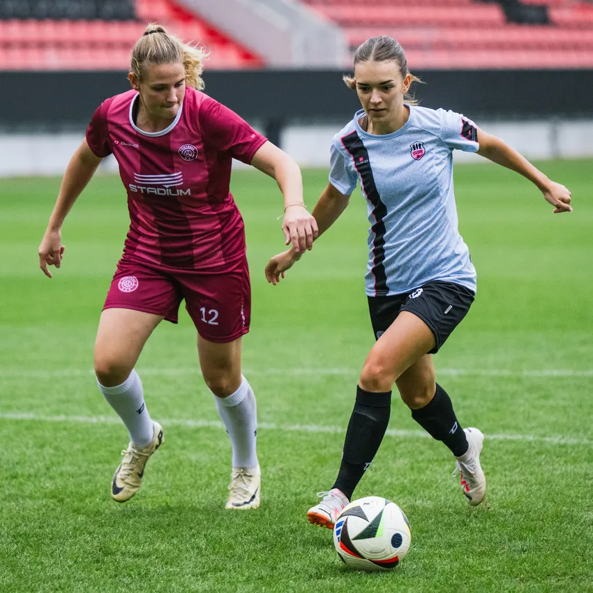 Dos mujeres en ropa deportiva juegan al fútbol en un campo verde.