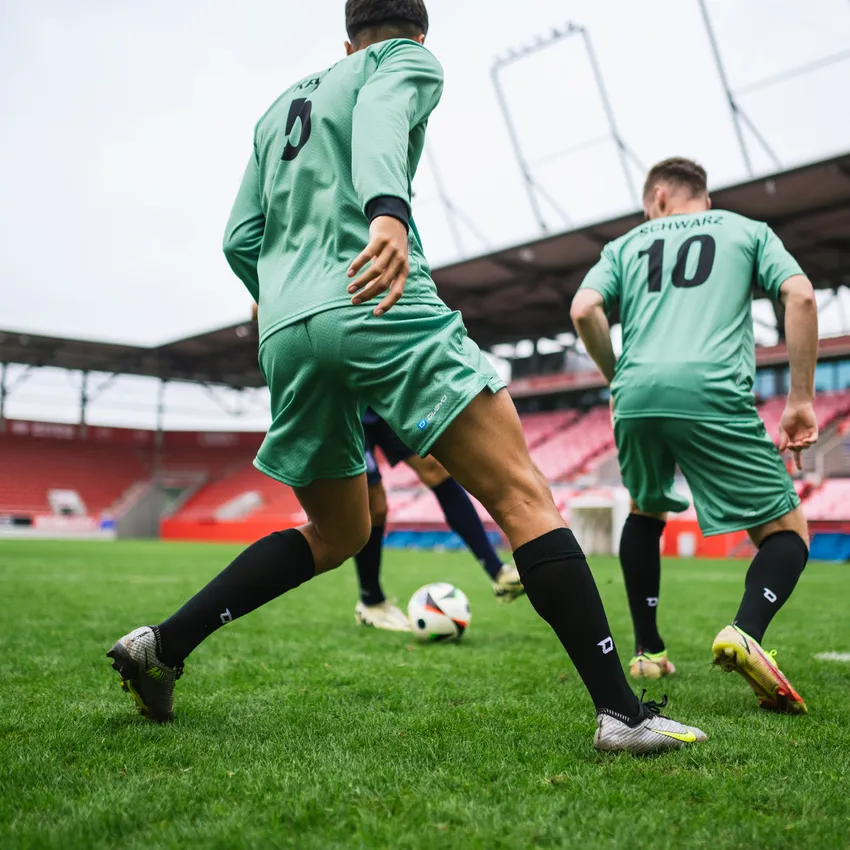Dos jugadores con camisetas de fútbol verdes y calcetas negras jugando en un campo en un estadio.