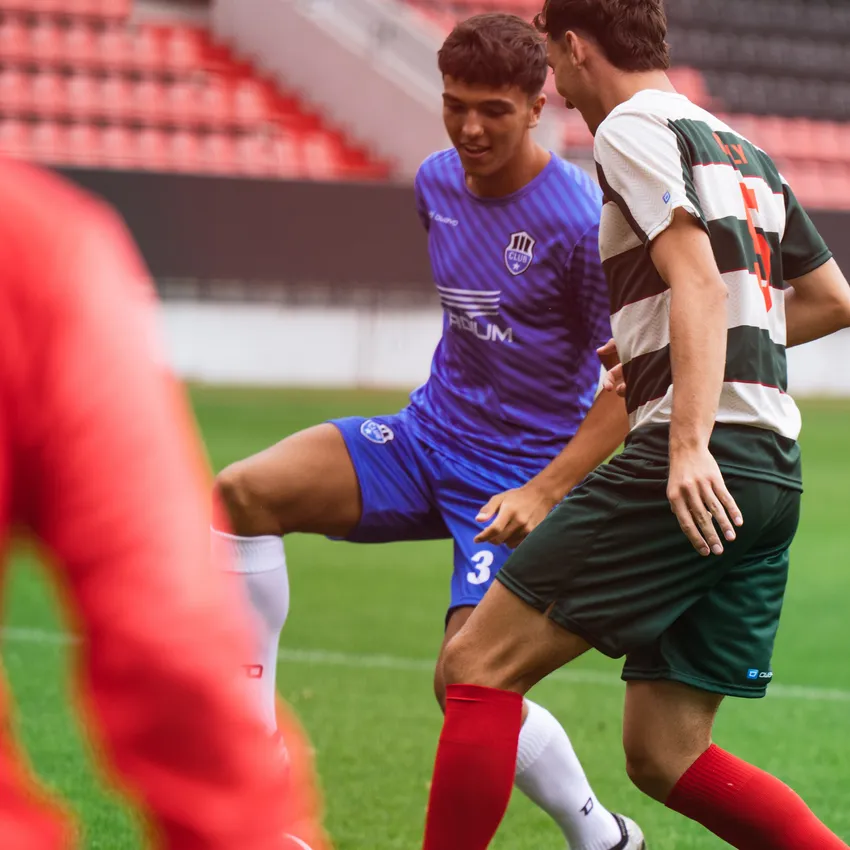 Dos futbolistas en acción en el campo, uno con una camiseta azul y el otro con una camiseta a rayas verdes y rojas.