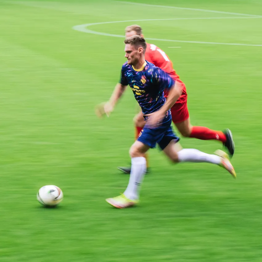 Un jugador de fútbol con una camiseta colorida corre por el campo mientras otro jugador lo persigue.