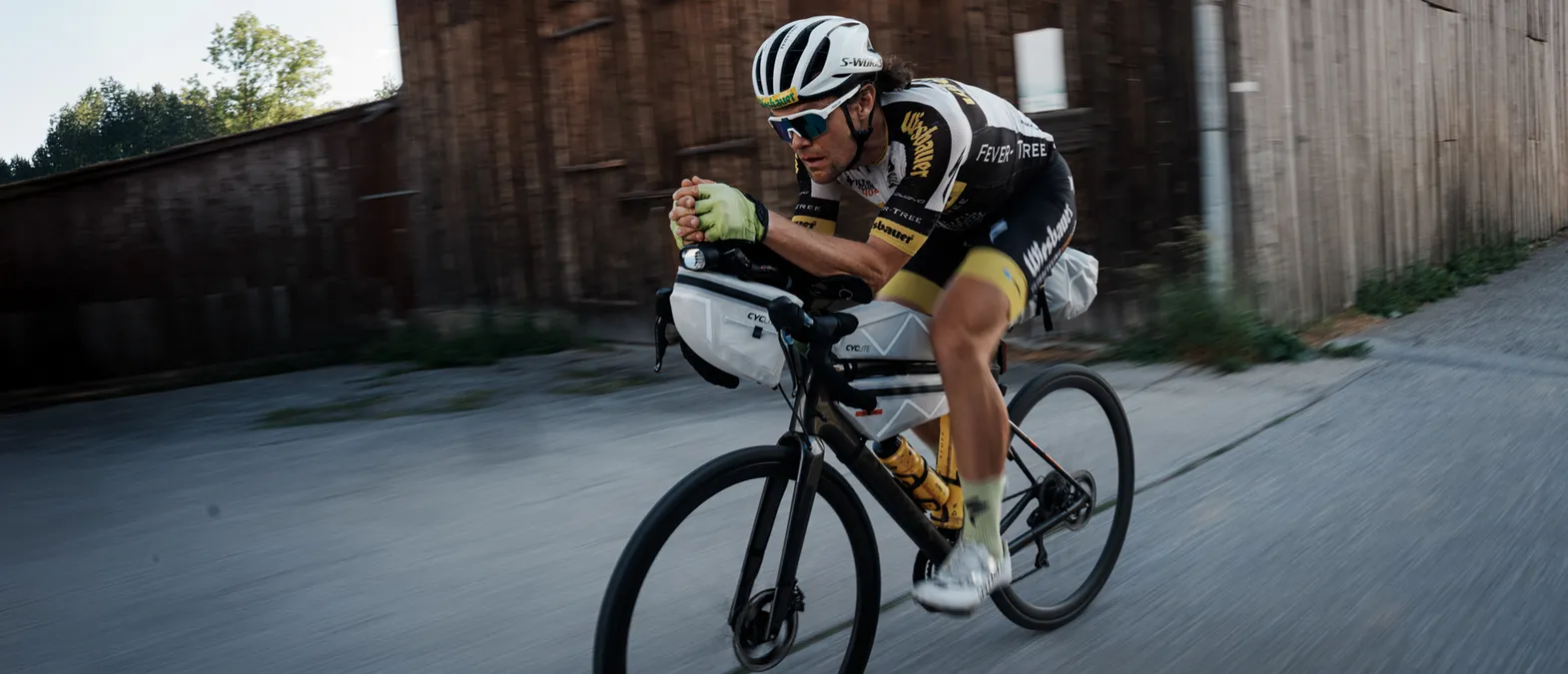 Un ciclista en posición aerodinámica sobre una bicicleta de carretera, usando ropa deportiva personalizada de owayo, mientras pedalea por una calle.