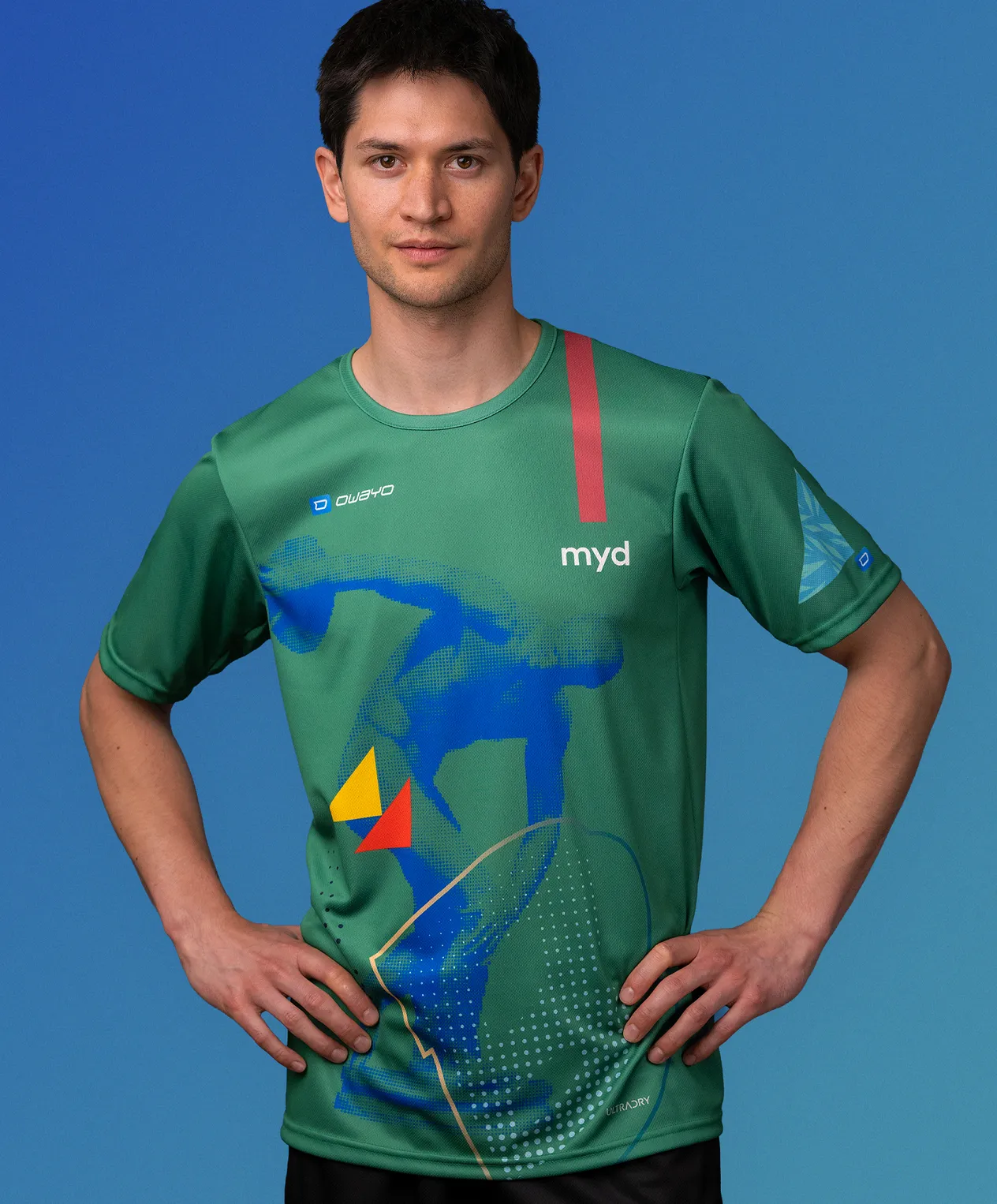 Un hombre vistiendo una camiseta deportiva verde personalizada de owayo con un diseño gráfico azul, amarillo y rojo y la palabra 'myd' en el pecho.