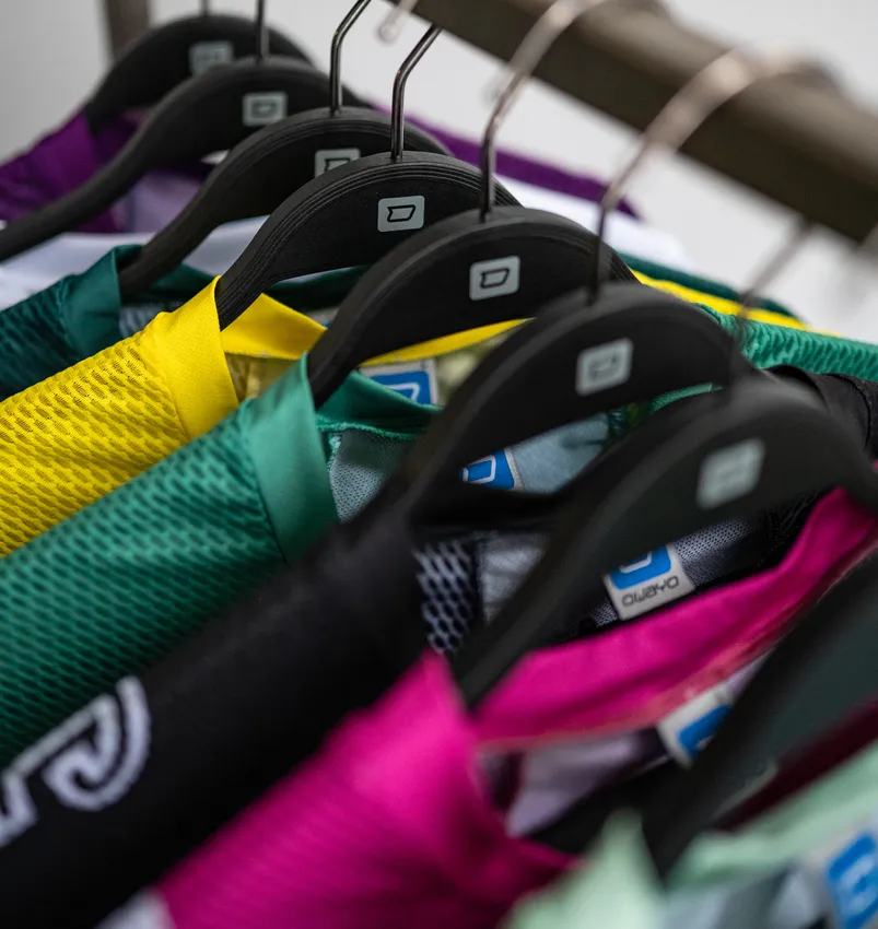 Varios artículos de ropa deportiva personalizados de colores cuelgan de perchas negras.
