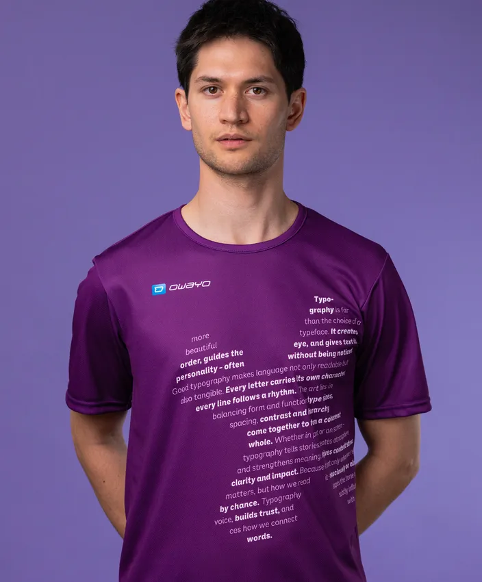 Un hombre lleva una camiseta deportiva morada con texto tipográfico en la parte delantera, frente a un fondo morado.