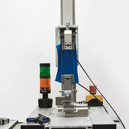 Un tejido azul está siendo probado en una máquina sobre una mesa de trabajo, junto a una luz de señalización y herramientas.