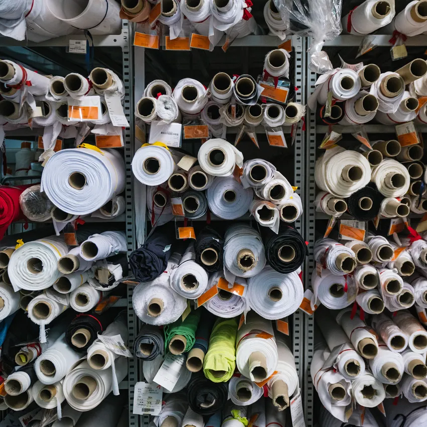 Estantes llenos de rollos de tela en varios colores y tamaños, utilizados para la fabricación de ropa deportiva.