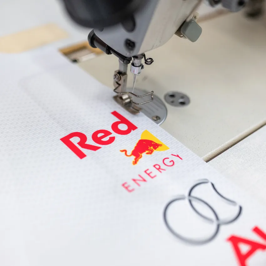 Una máquina de coser que está cosiendo en una tela blanca con logotipos coloridos.