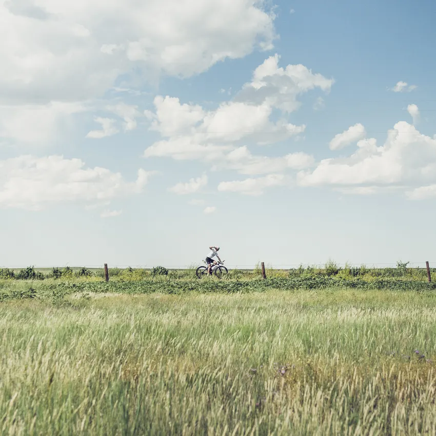Una persona monta en bicicleta a través de un paisaje verde bajo un cielo azul con algunas nubes.