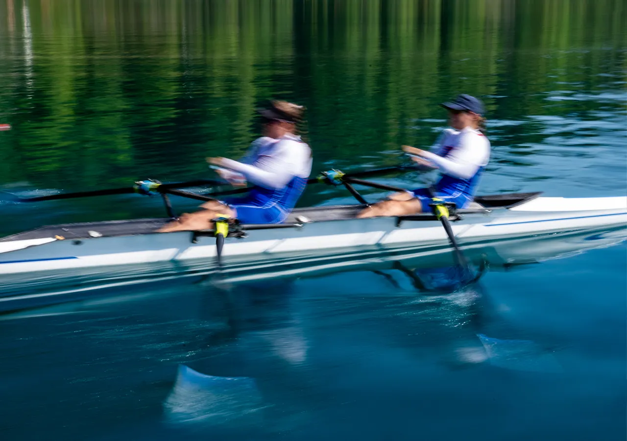 Dos remeros con ropa deportiva azul reman al unísono en una superficie de agua tranquila.