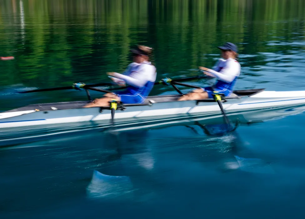 Dos remeros con ropa deportiva azul reman al unísono en aguas tranquilas.
