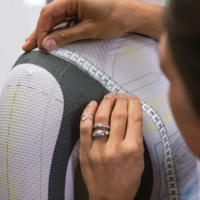 Una persona mide el brazo superior de una prenda deportiva personalizada de owayo, marcada con líneas de corte.