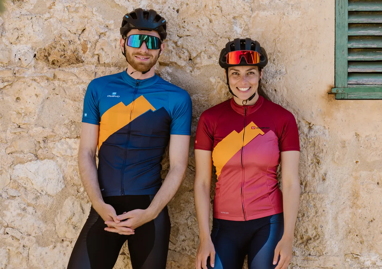 Un hombre y una mujer con ropa deportiva personalizada de owayo, de pie frente a una pared de piedra.