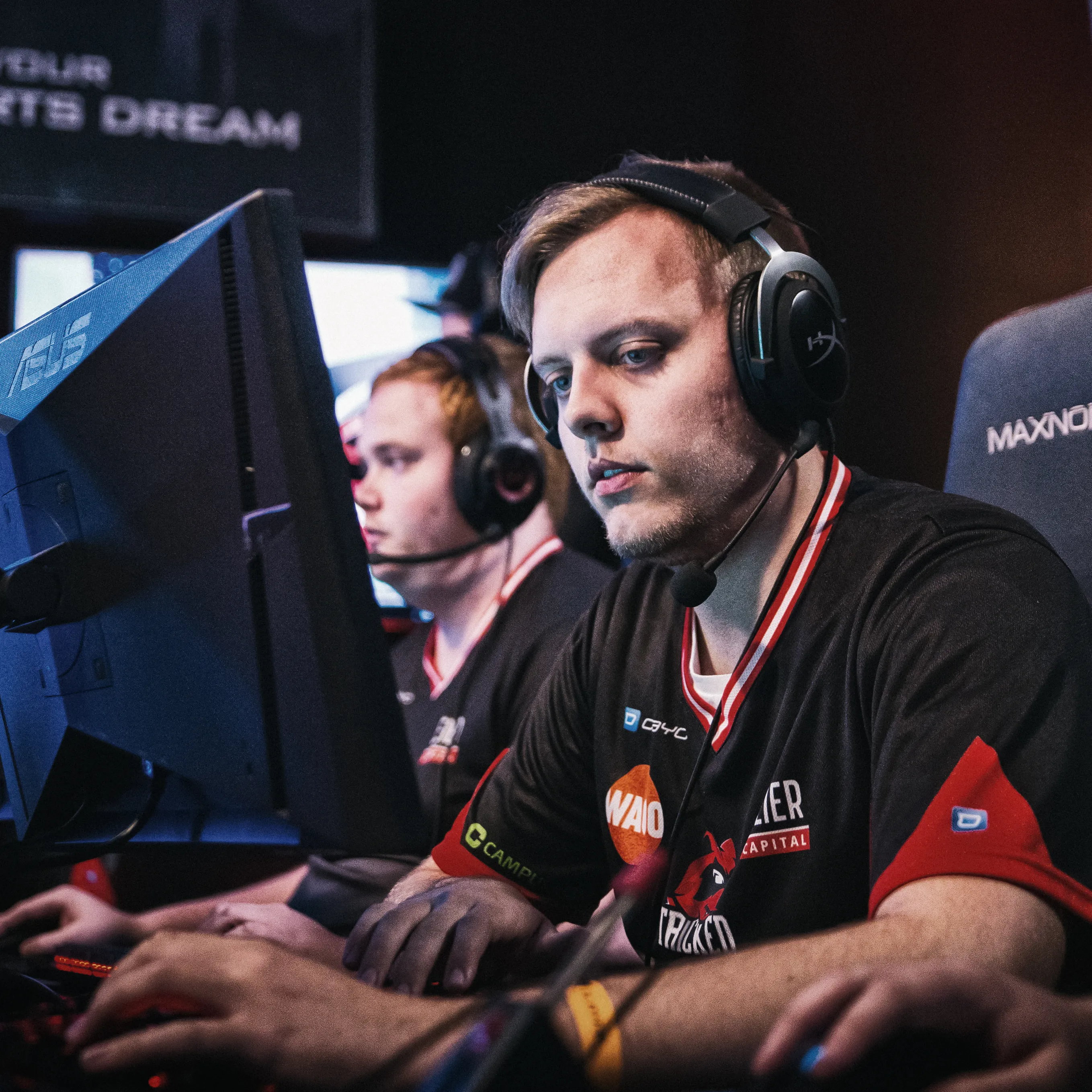 Dos jugadores en camisetas deportivas con auriculares, concentrados en sus computadoras durante un torneo de eSports.