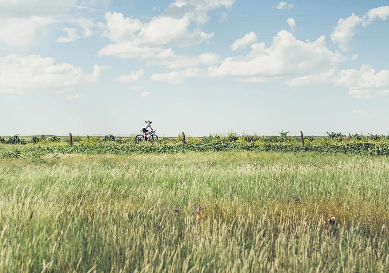 Una persona monta en bicicleta a través de un campo verde bajo un cielo azul con nubes blancas.
